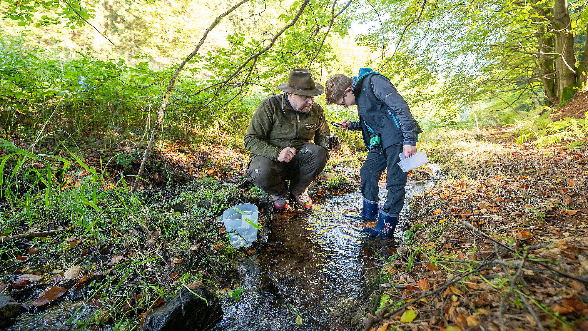 Ranger und Kind im Bergbach untersuchen Steine