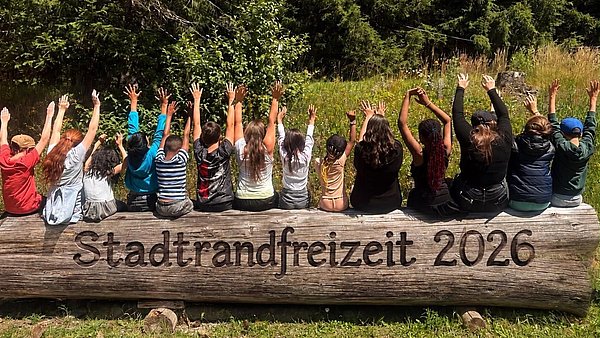 Kinder sitzen auf einem Baumstamm am Waldrand