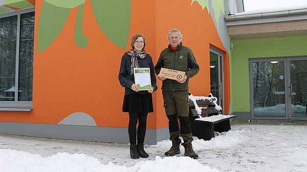 zwei Personen vor einem Haus mit der Urkunde Biosphärenpartner